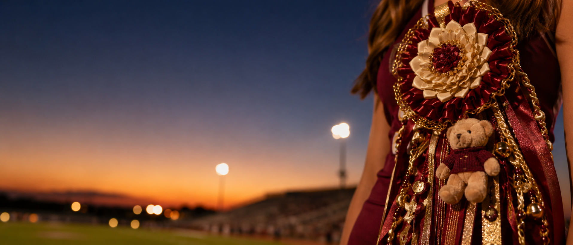 Maroon and gold handcrafted homecoming mum at a Friday night football stadium during sunset